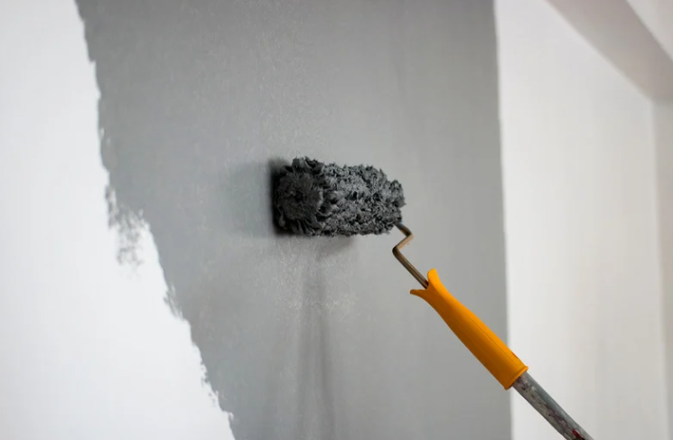 A paint roller with a yellow handle applying gray paint to a white wall.